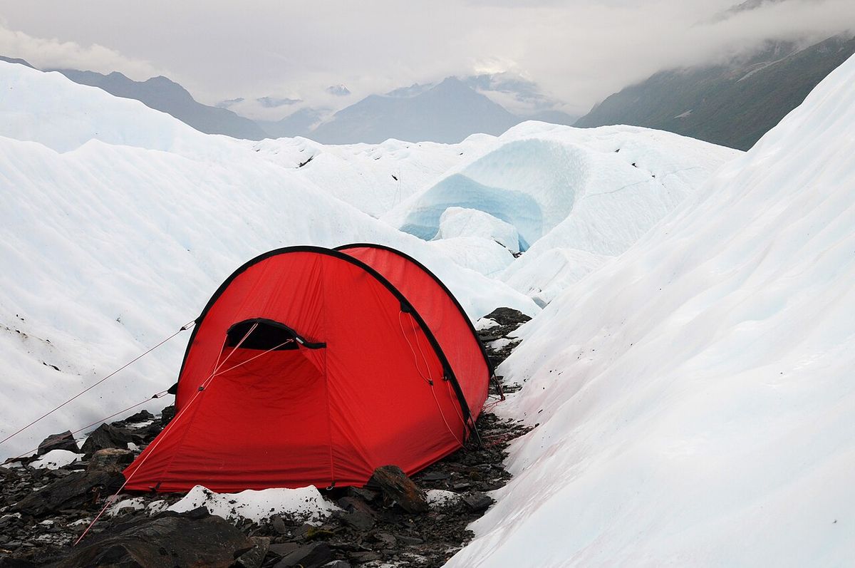 A red Hilleberg Nammatj 2 tunnel tent guyed out on rocks between ice ridges on a glacier