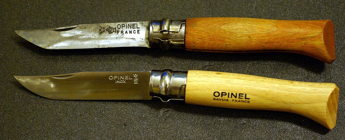 Two Opinel No. 8 folding knives: a well-used carbon-steel one above a new stainless Inox one with a plain beechwood handle