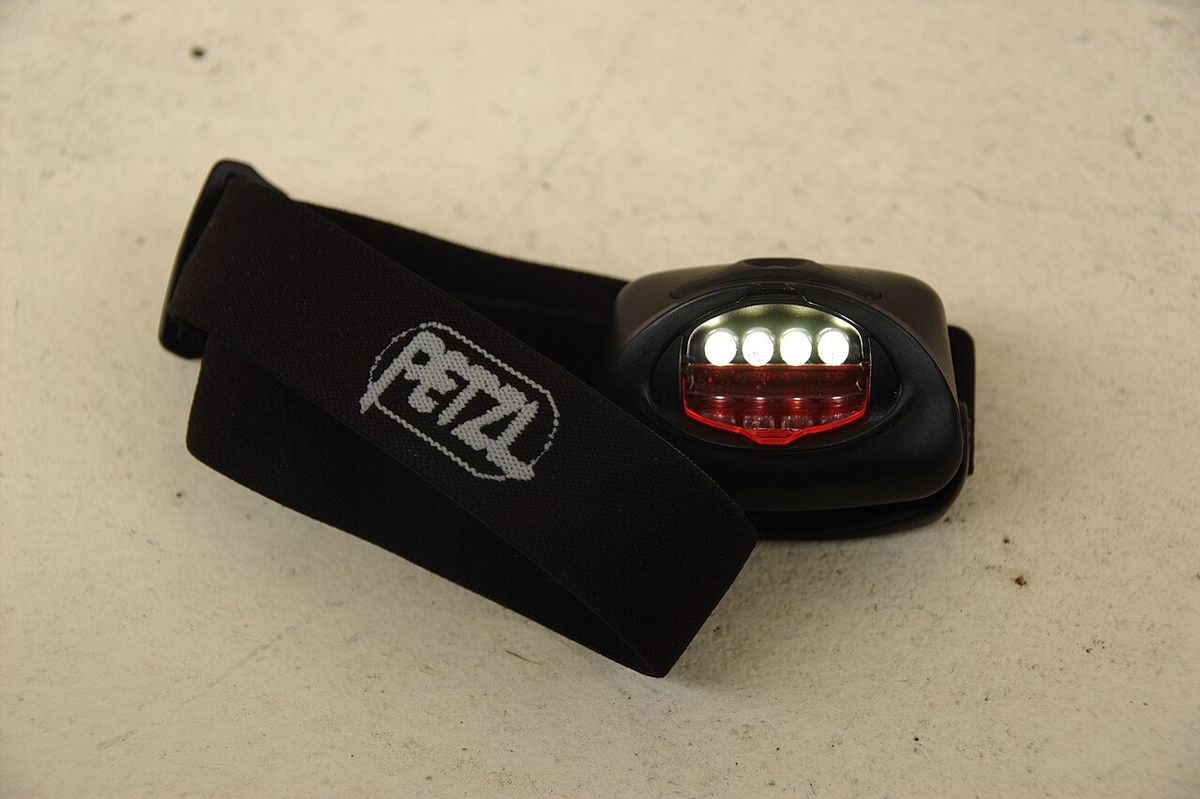An older Petzl Tikka headlamp with four white LEDs and a red lens on its elastic strap