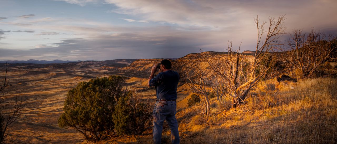 A hiker scanning a golden valley at dusk from a rocky overlook